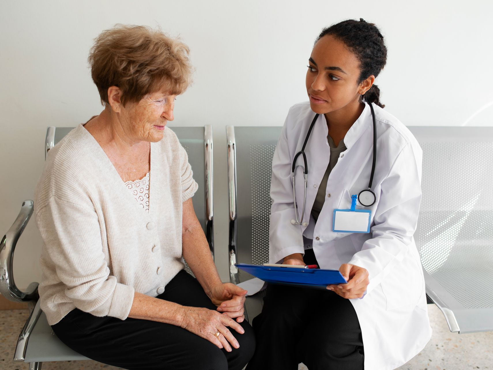 A healthcare professional in a white coat with a stethoscope reviews a document with a seated patient in a clinical room.