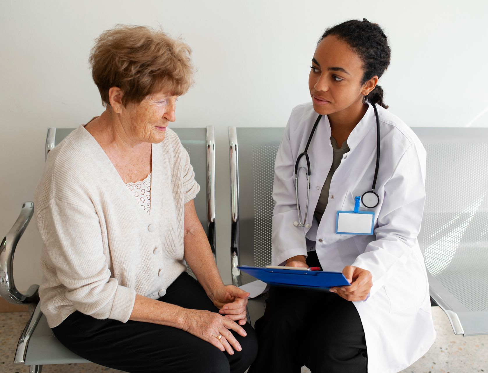 A medical professional in a white coat with a stethoscope reviews a document while sitting next to a patient.