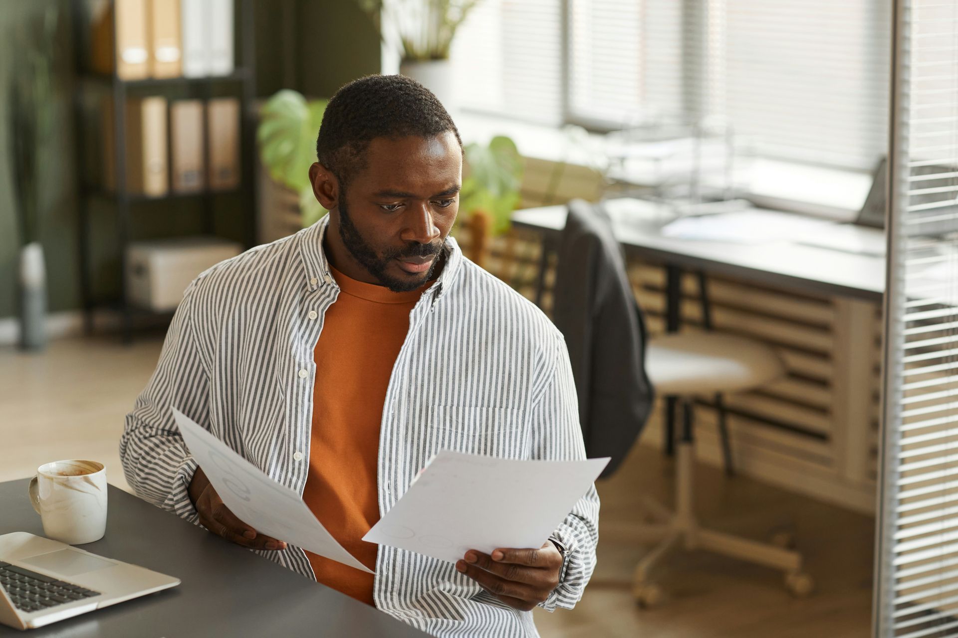 A focused professional in a striped shirt sits at a desk, reviewing documents in a bright, modern home office.