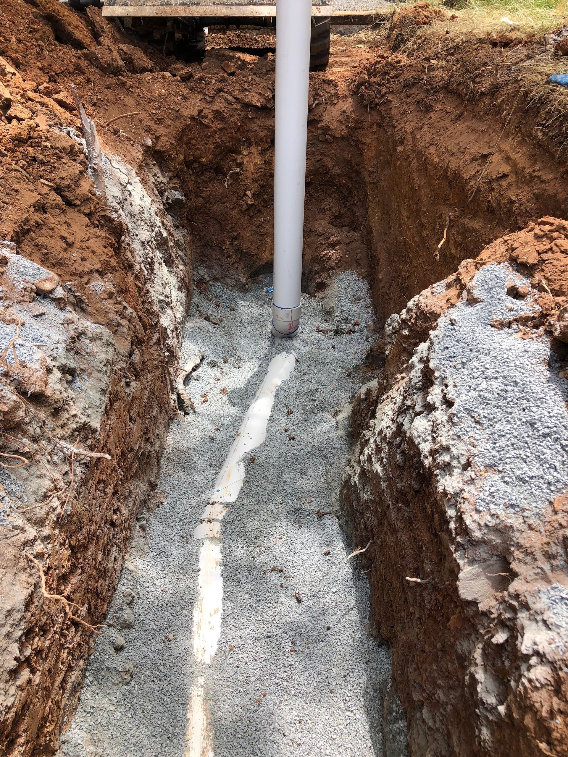 Excavated trench with a vertical pipe and gravel-filled base between dirt — Plumbing in Canberra, ACT
