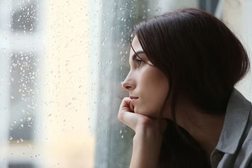 A woman is looking out of a window on a rainy day.