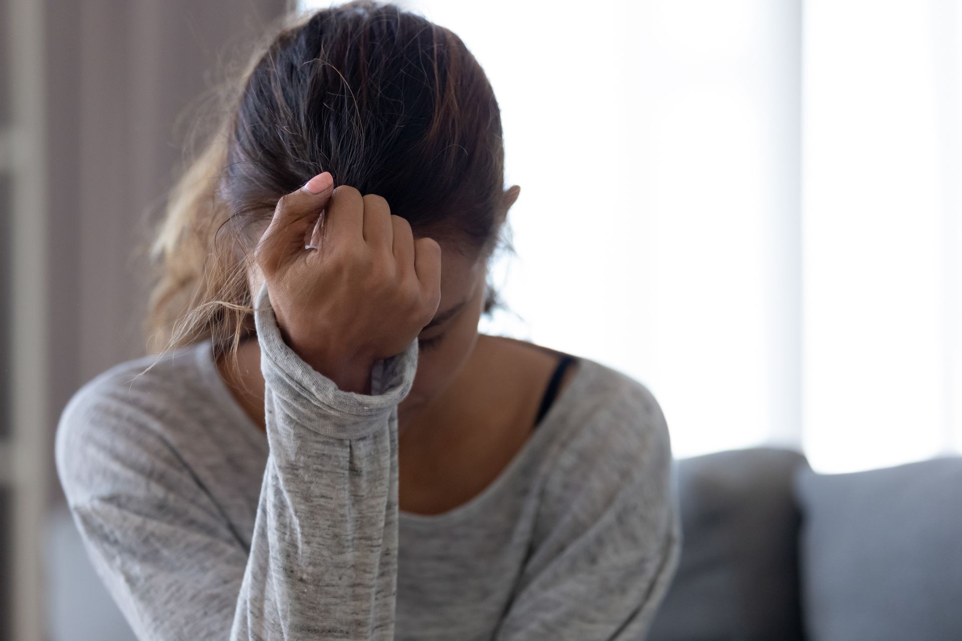 A woman is sitting on a couch covering her face with her hand.