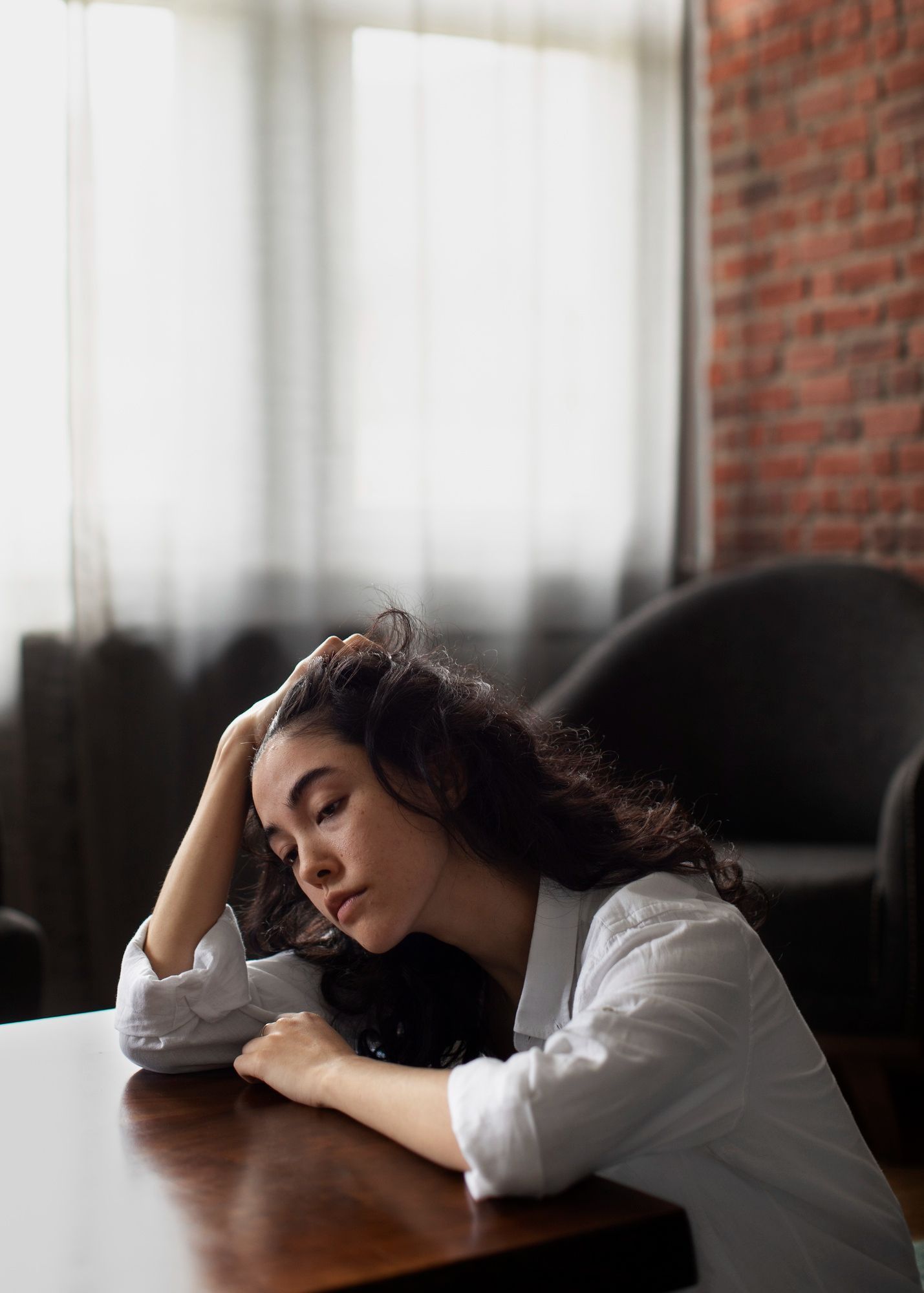 A woman is sitting at a table with her head resting on her hand.