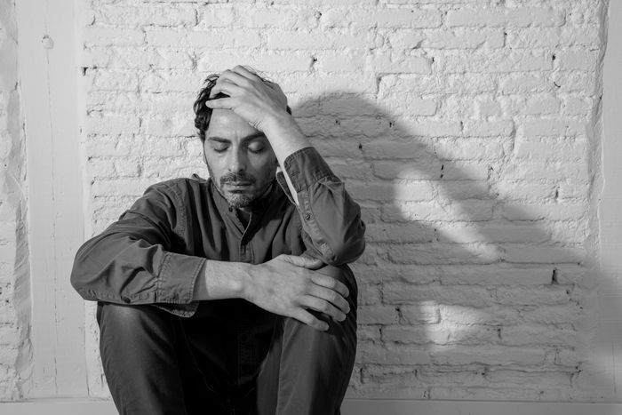 A man is sitting in front of a brick wall with his head in his hands.