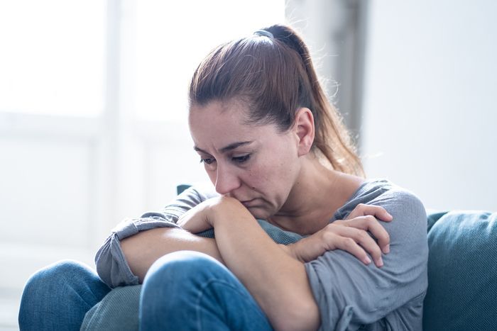 A woman is sitting on a couch with her head on her knees.