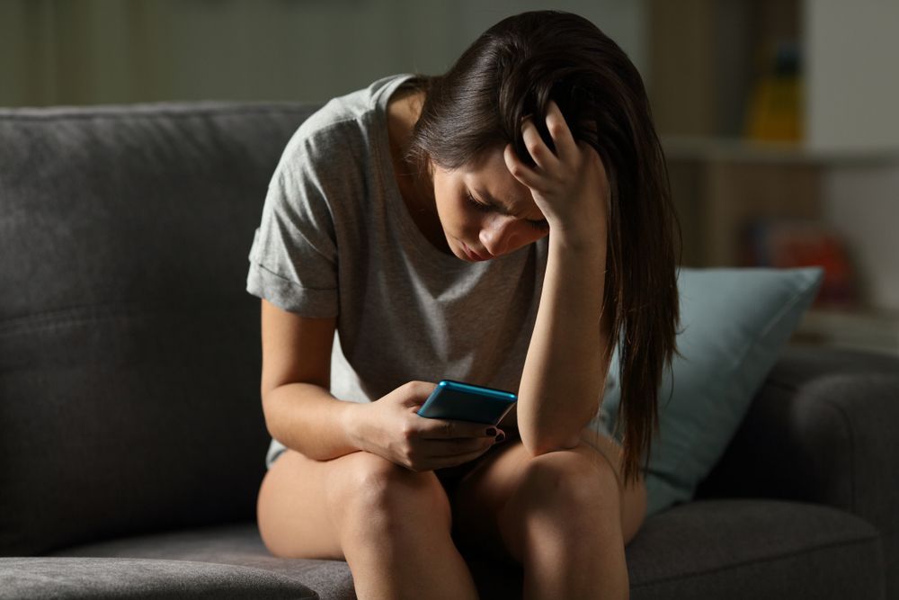 A woman is sitting on a couch looking at her phone.