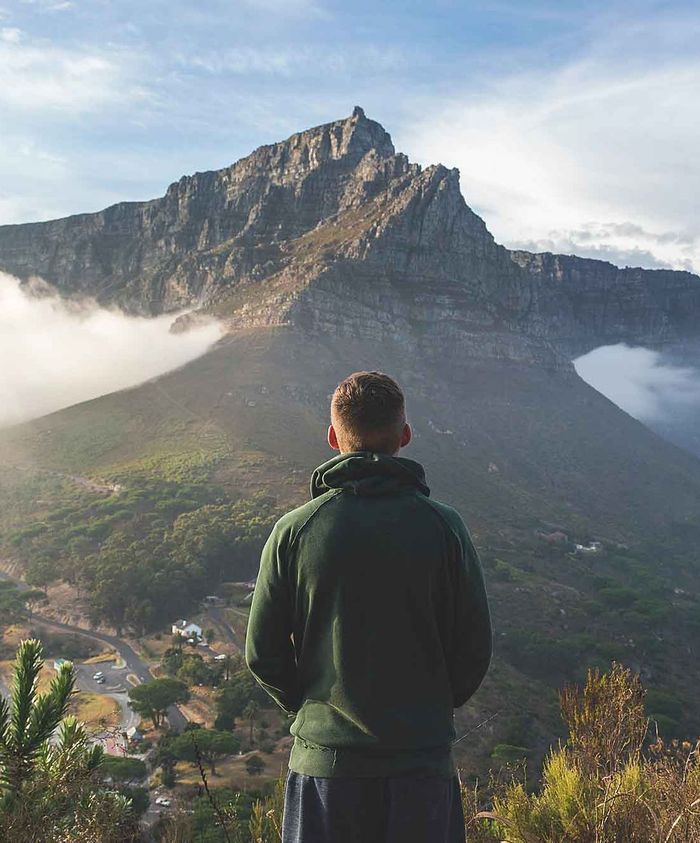 A man is standing on top of a mountain looking at the view.