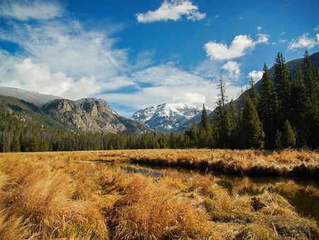 A river runs through a grassy field with mountains in the background.