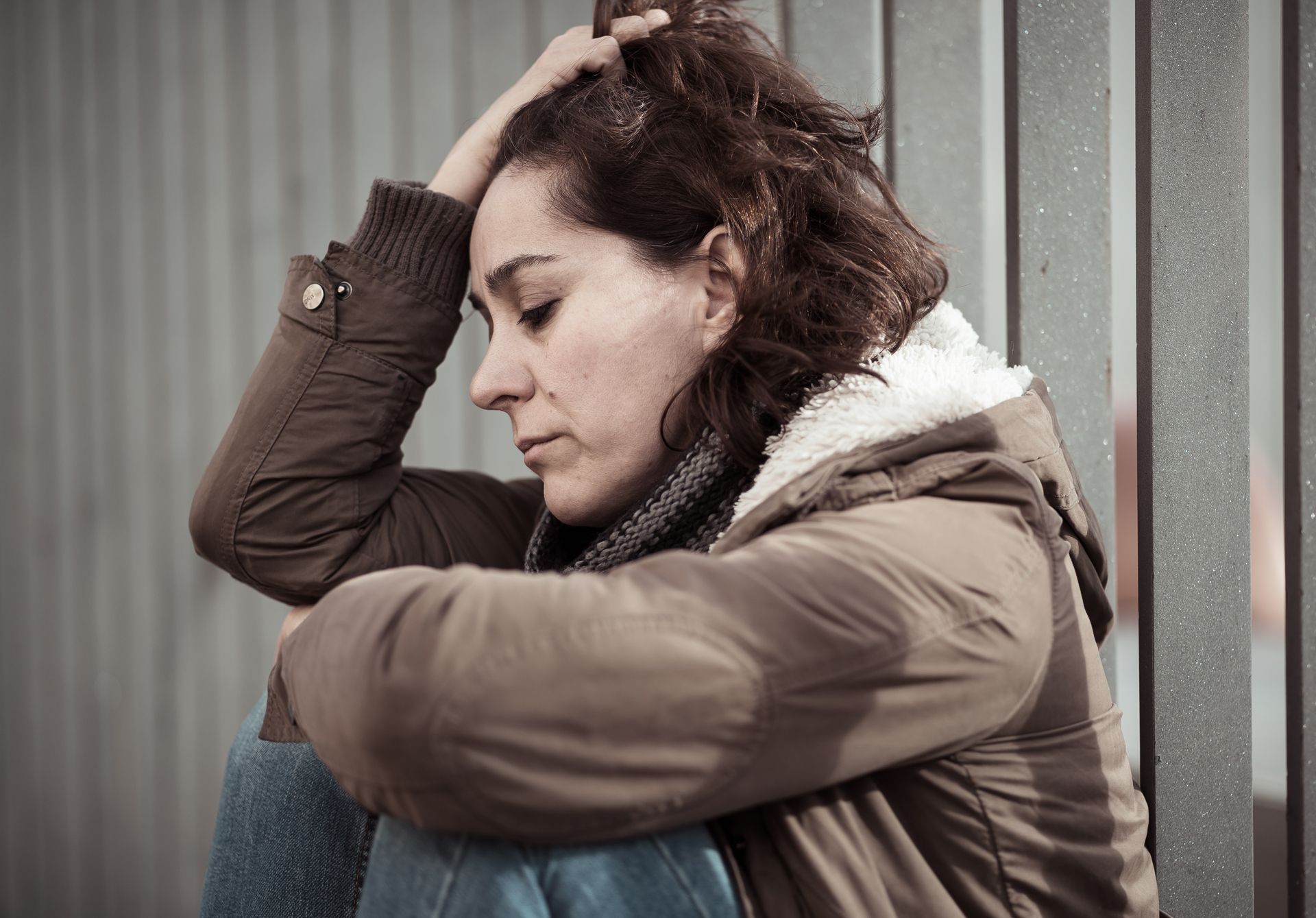 A woman is sitting on the ground with her head in her hands.