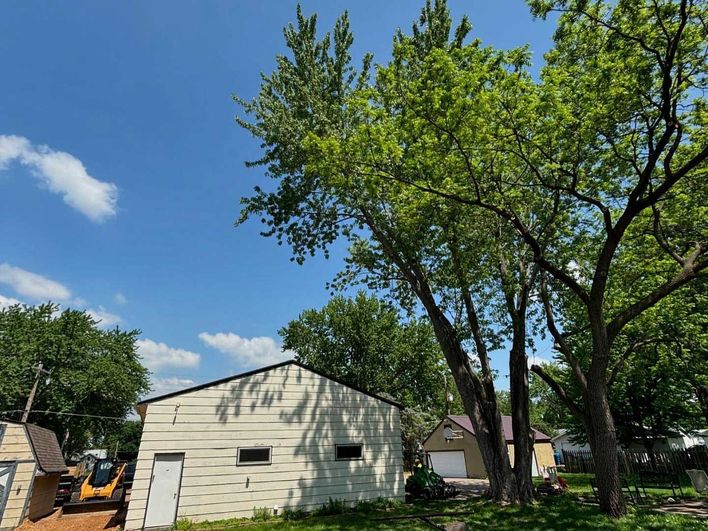 A white garage with a yellow excavator parked in front of it.