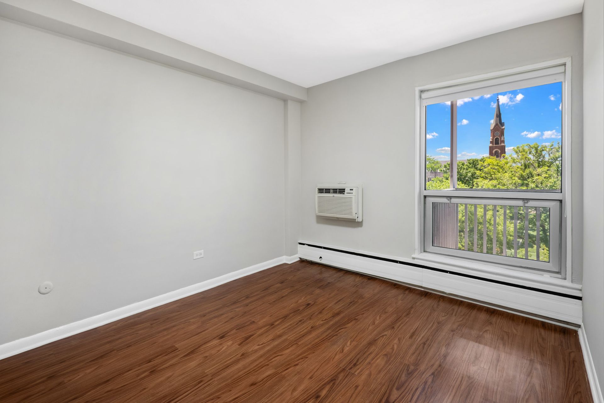 An empty room with hardwood floors and a window with a view of a clock tower  at Reside on North Park.