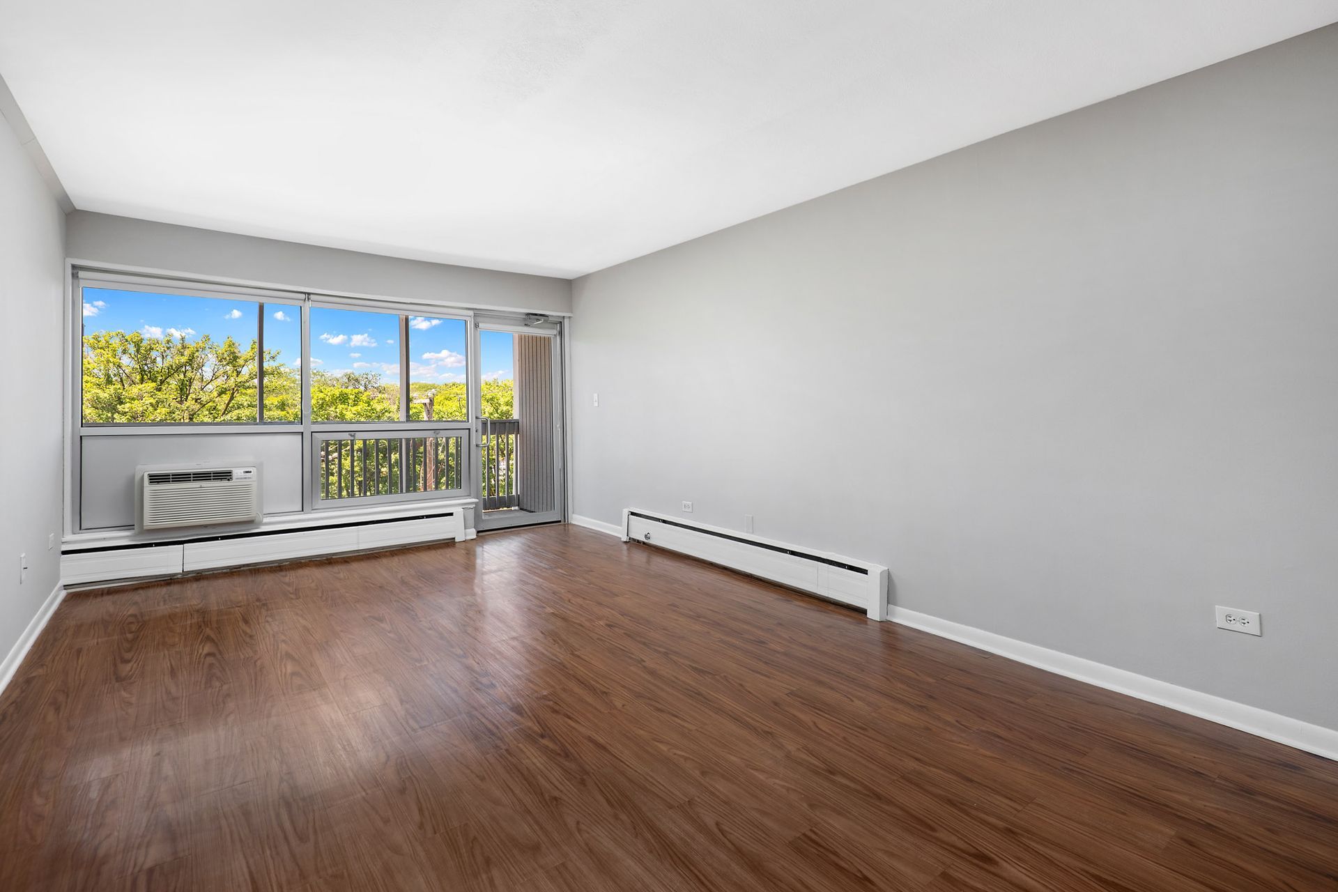 An empty living room with hardwood floors and a balcony at Reside on North Park.