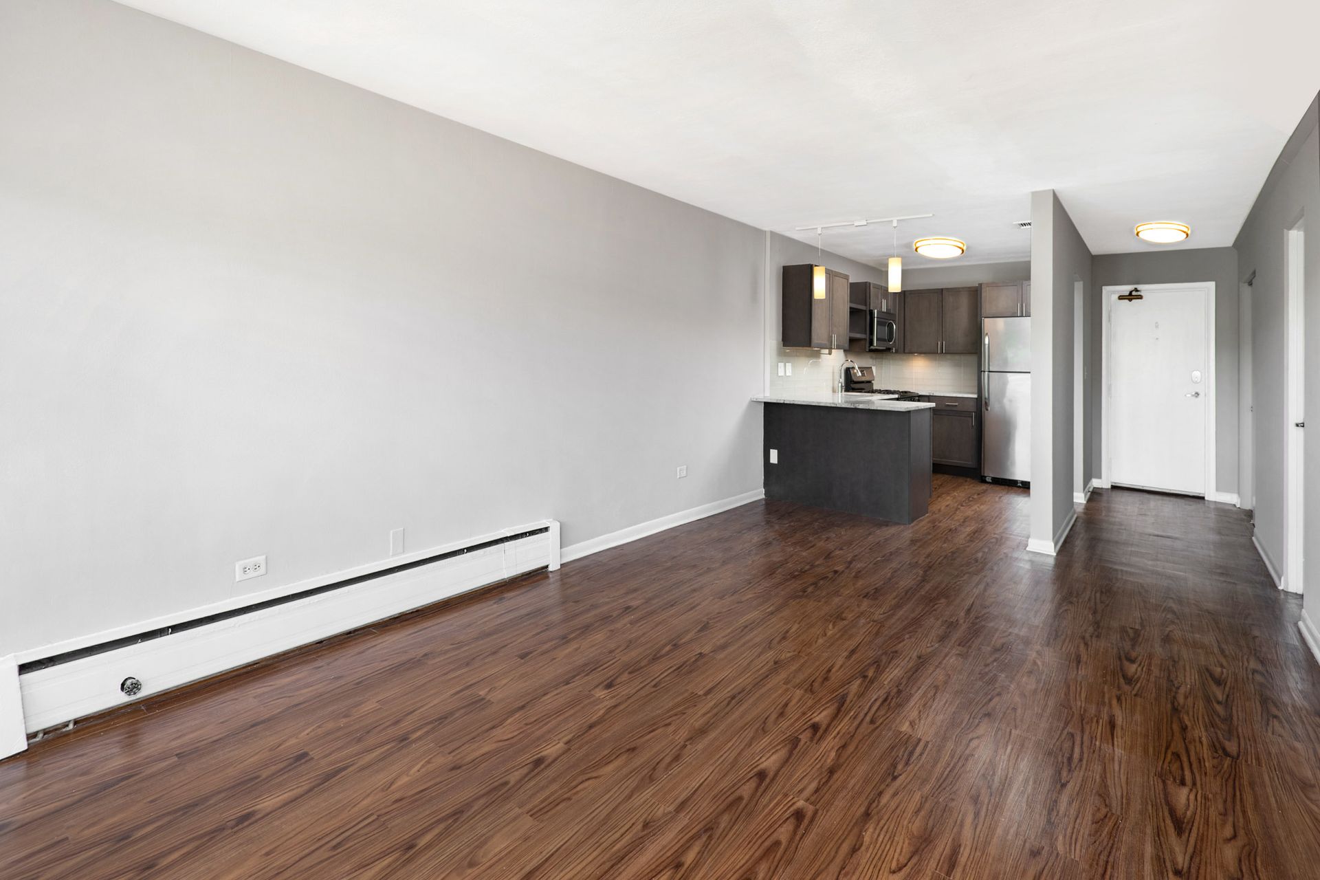 An empty living room with hardwood floors and a kitchen in the background at Reside on North Park.