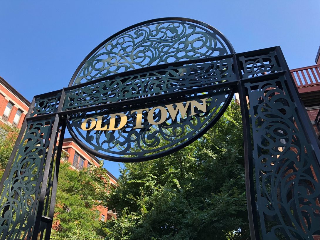 An old town sign is surrounded by trees and buildings