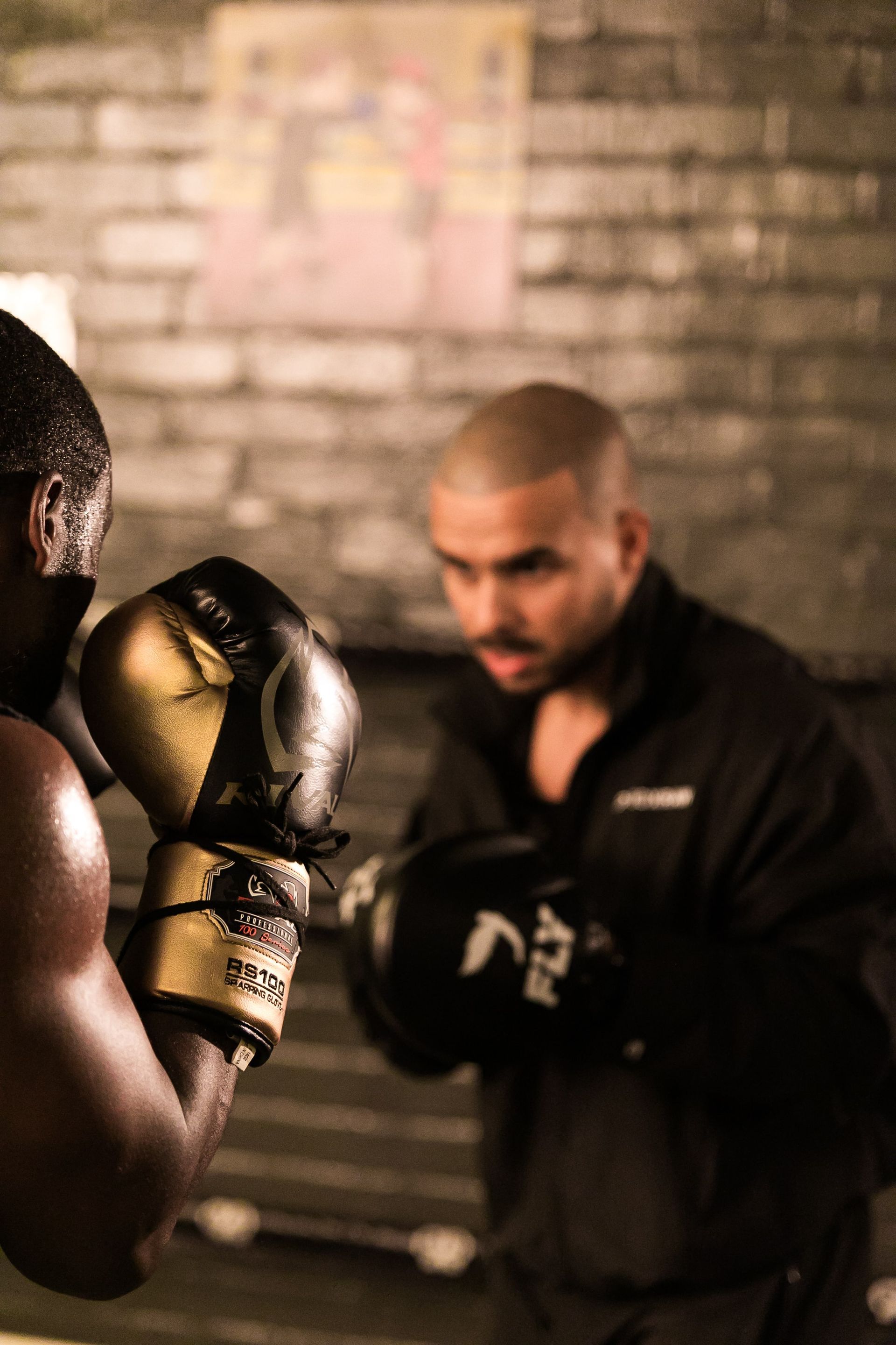 Two men wearing boxing gloves are practicing in a gym.