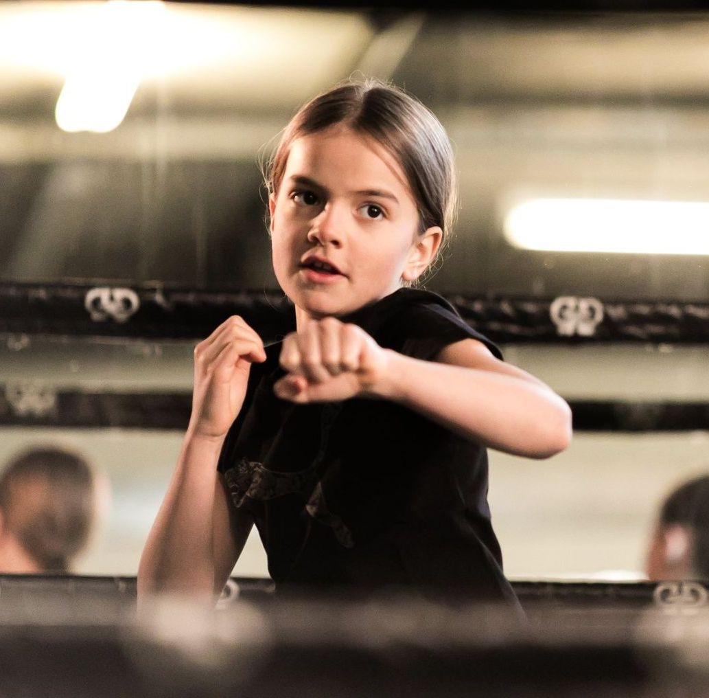 A young girl is standing in a boxing ring with the letter g on it