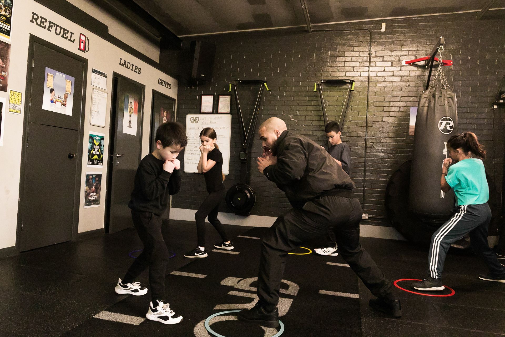 Coach Femi is teaching a group of children how to box in a gym.