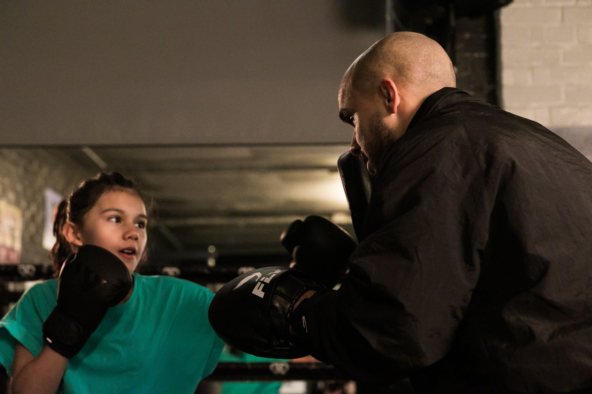 A man is teaching a young girl how to box in a gym.