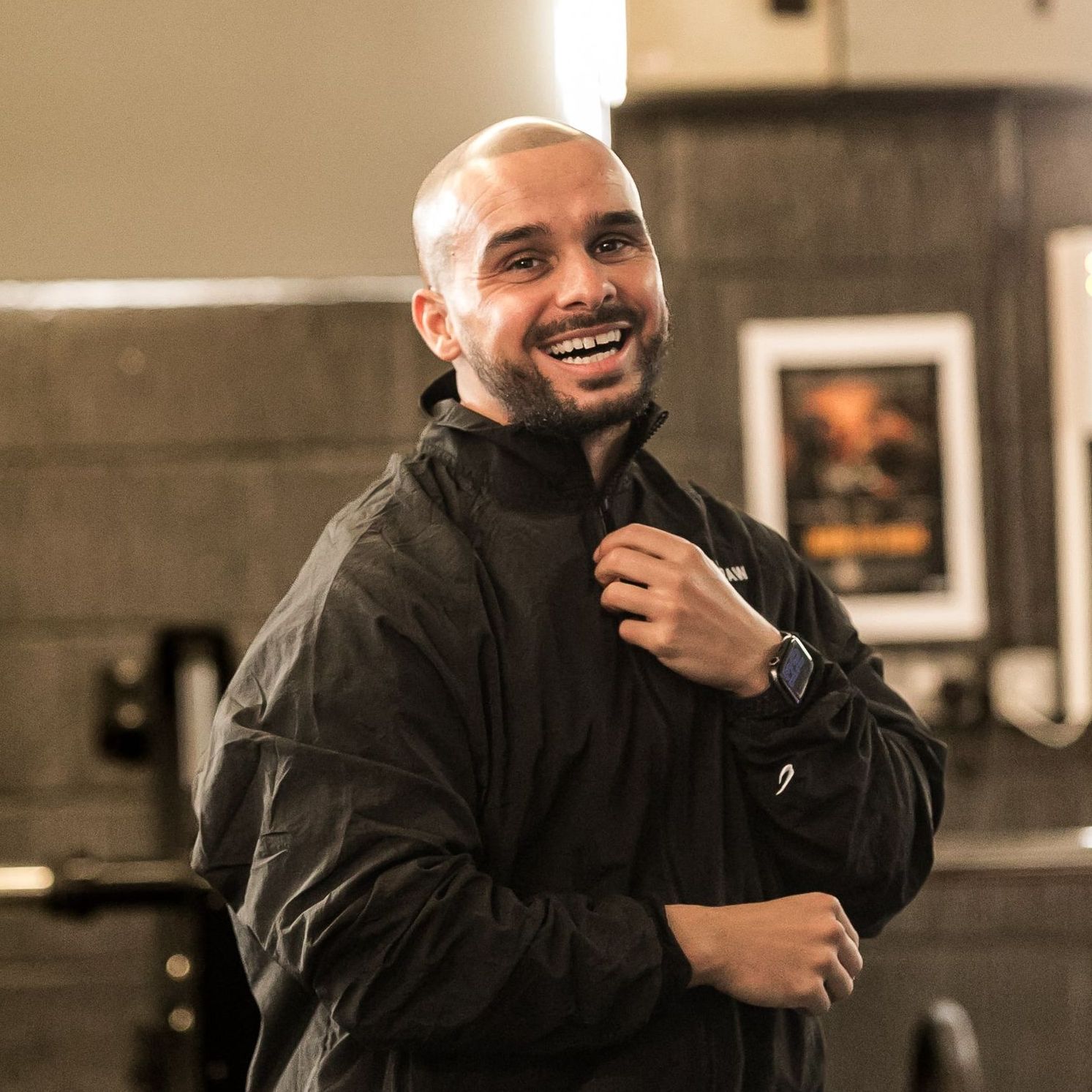 A man wearing a black jacket and a watch is smiling.
