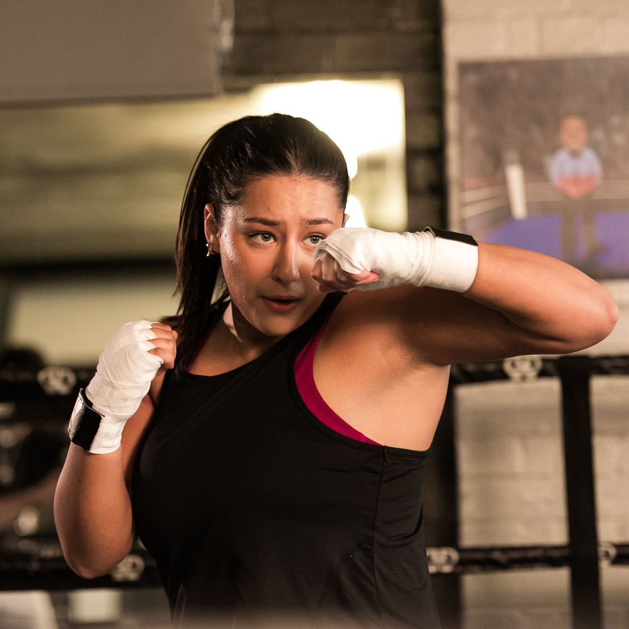 A woman wearing boxing gloves is standing in a boxing ring