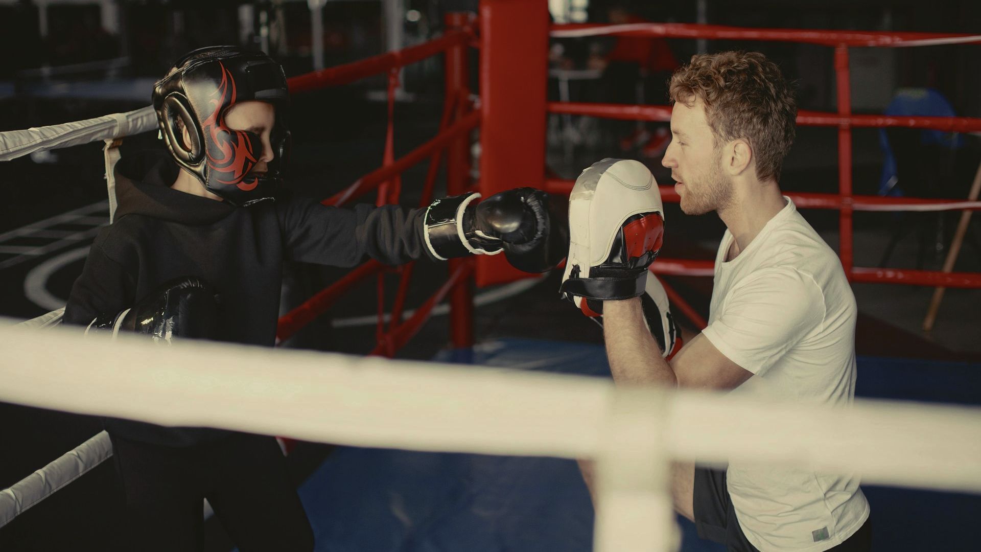 A man and a young prson are boxing in a boxing ring.