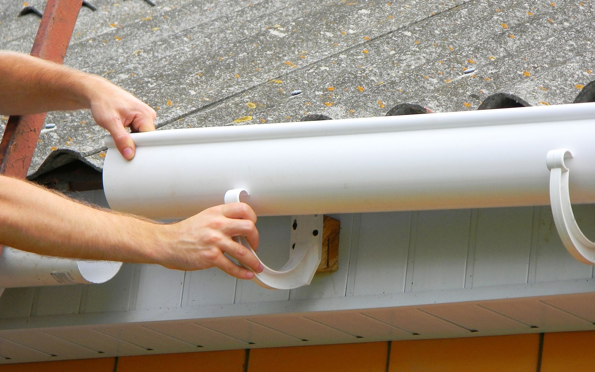 A person is installing a gutter on the side of a house.