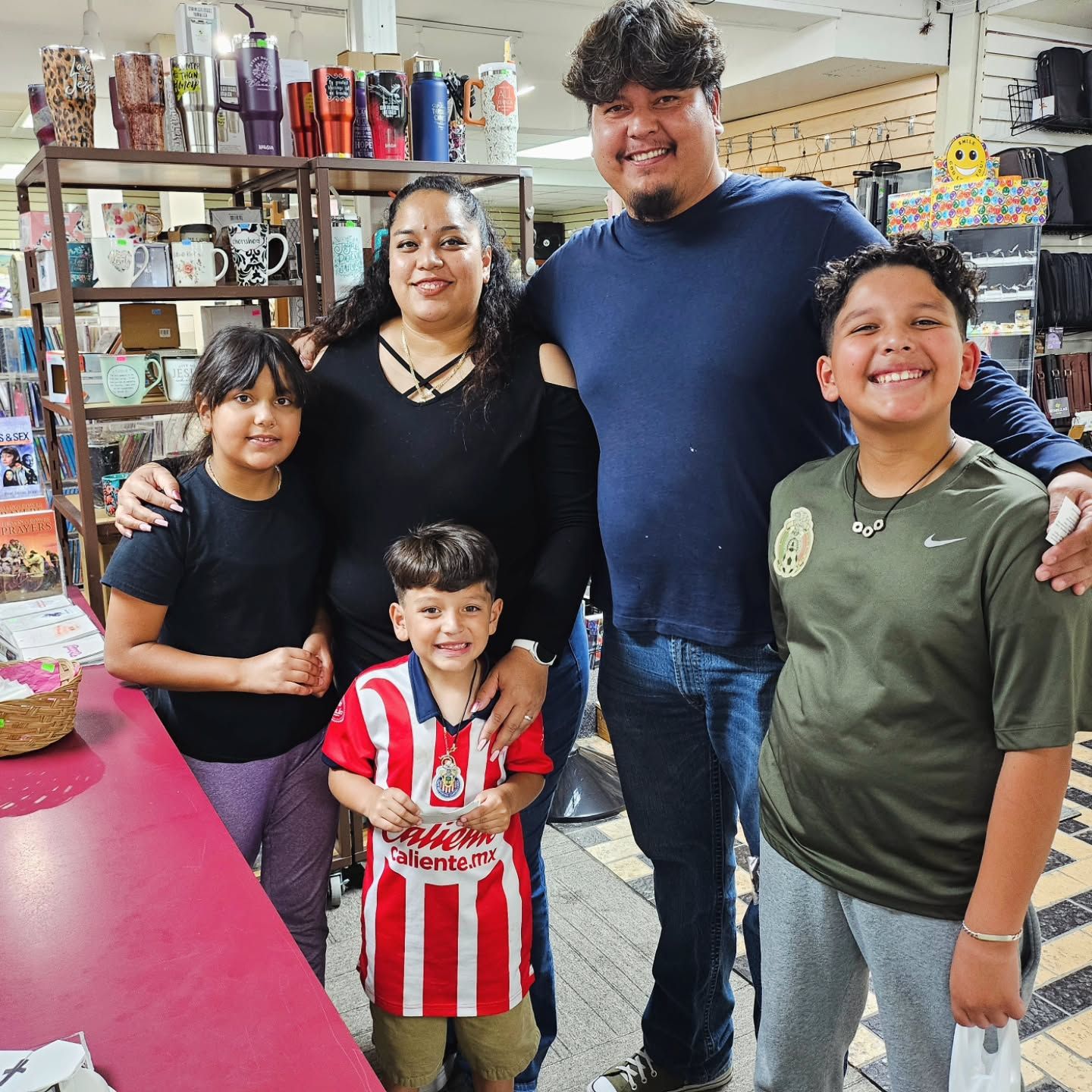 Family of five poses inside a store. Smiling, they stand near a counter and shelves of merchandise.