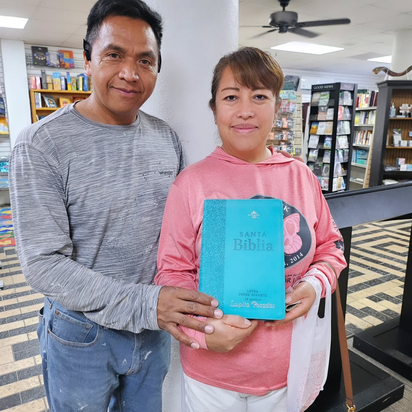 A man and woman in a bookstore holding a teal Spanish Bible; the woman smiles.