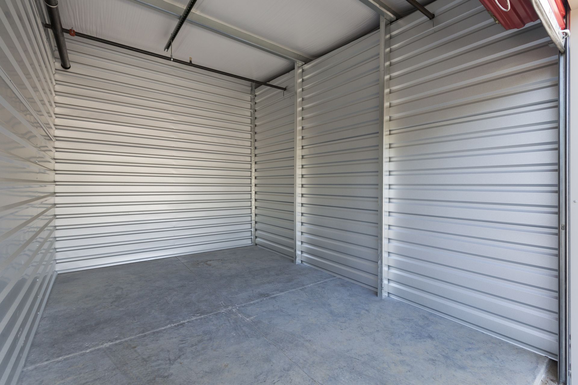 Empty metal storage unit with white corrugated walls and a concrete floor