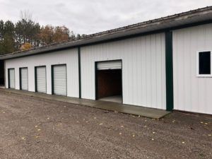 White metal warehouse with several garage doors and one open bay on a gravel lot