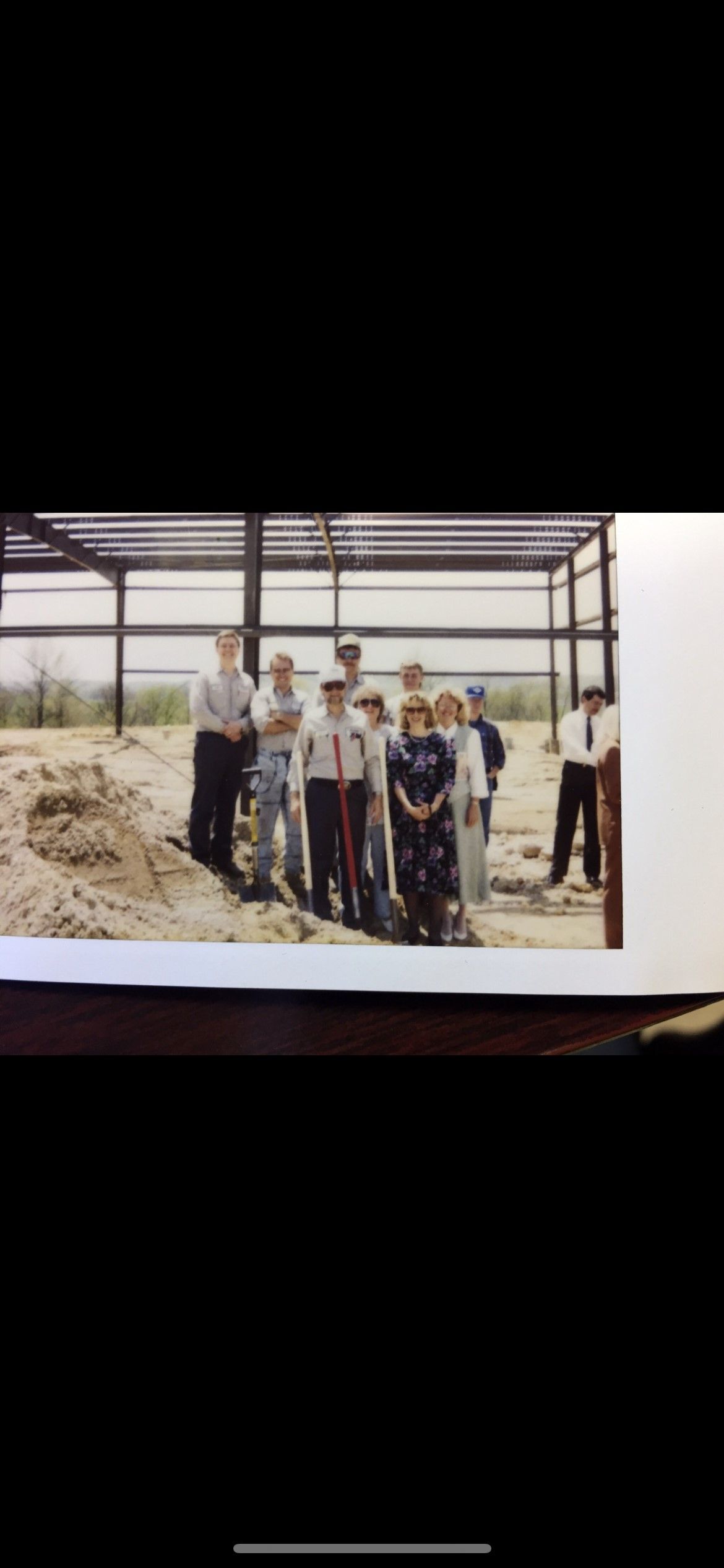 Group of people standing in front of a metal framed structure, possibly a building under construction.