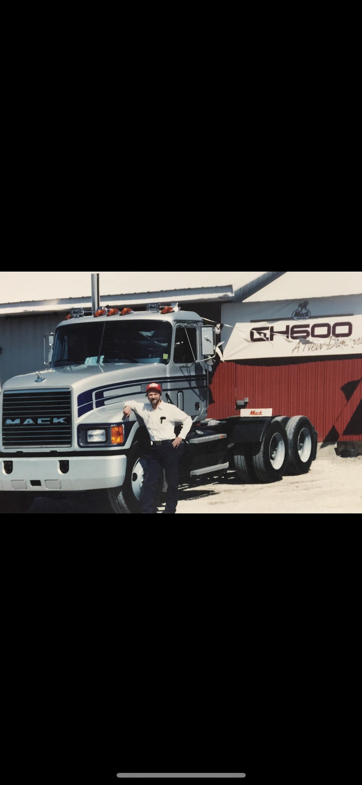 Man standing next to a silver Mack truck in front of a building.