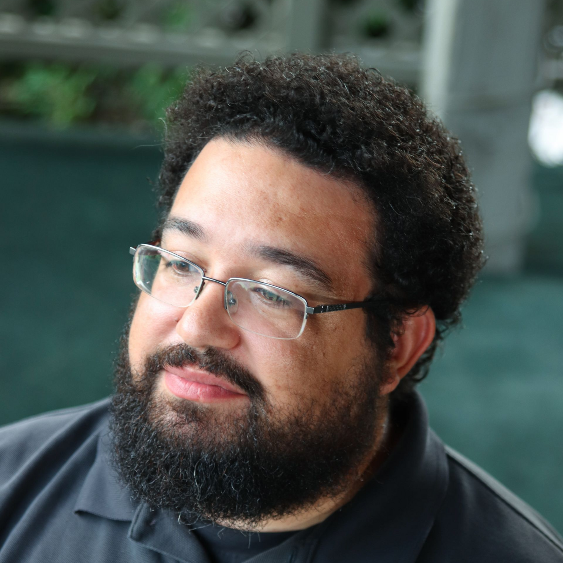 A bearded person wearing glasses looking off to the side.