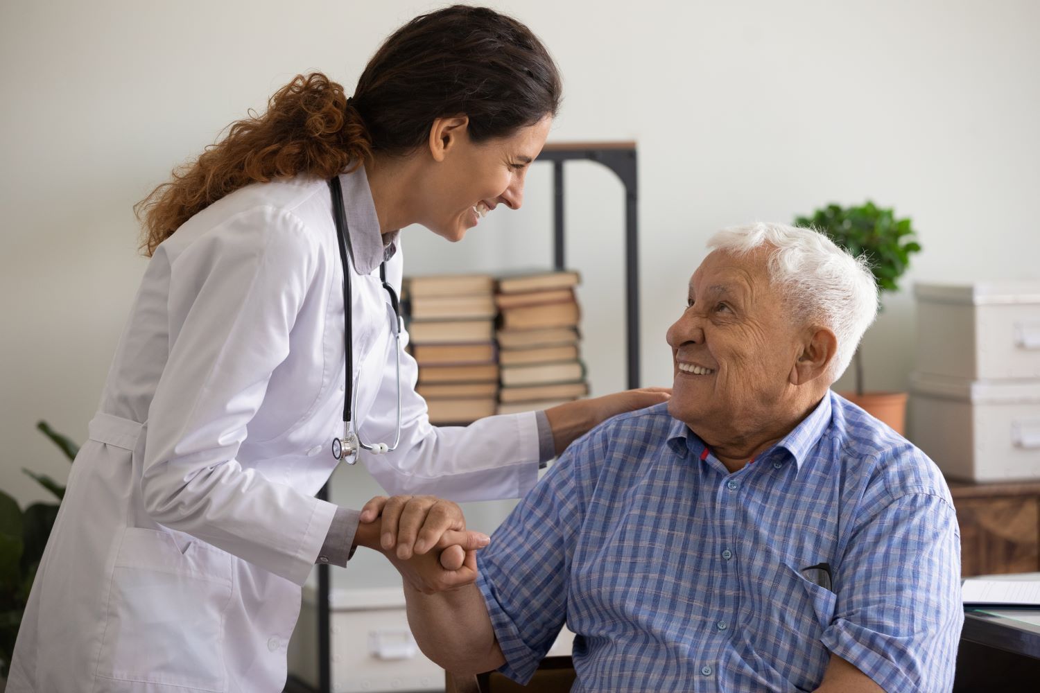 A doctor is holding the hand of an elderly man in a wheelchair.