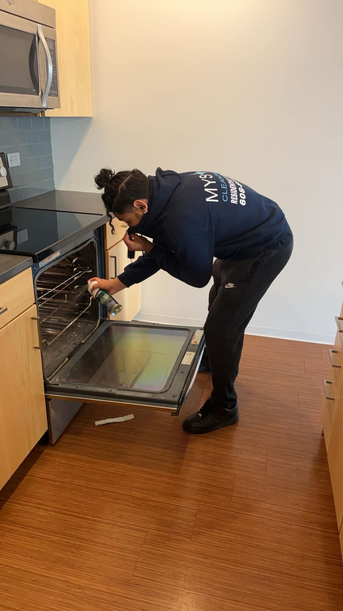 Person in blue hoodie leans into an oven in a kitchen, inspecting the interior.