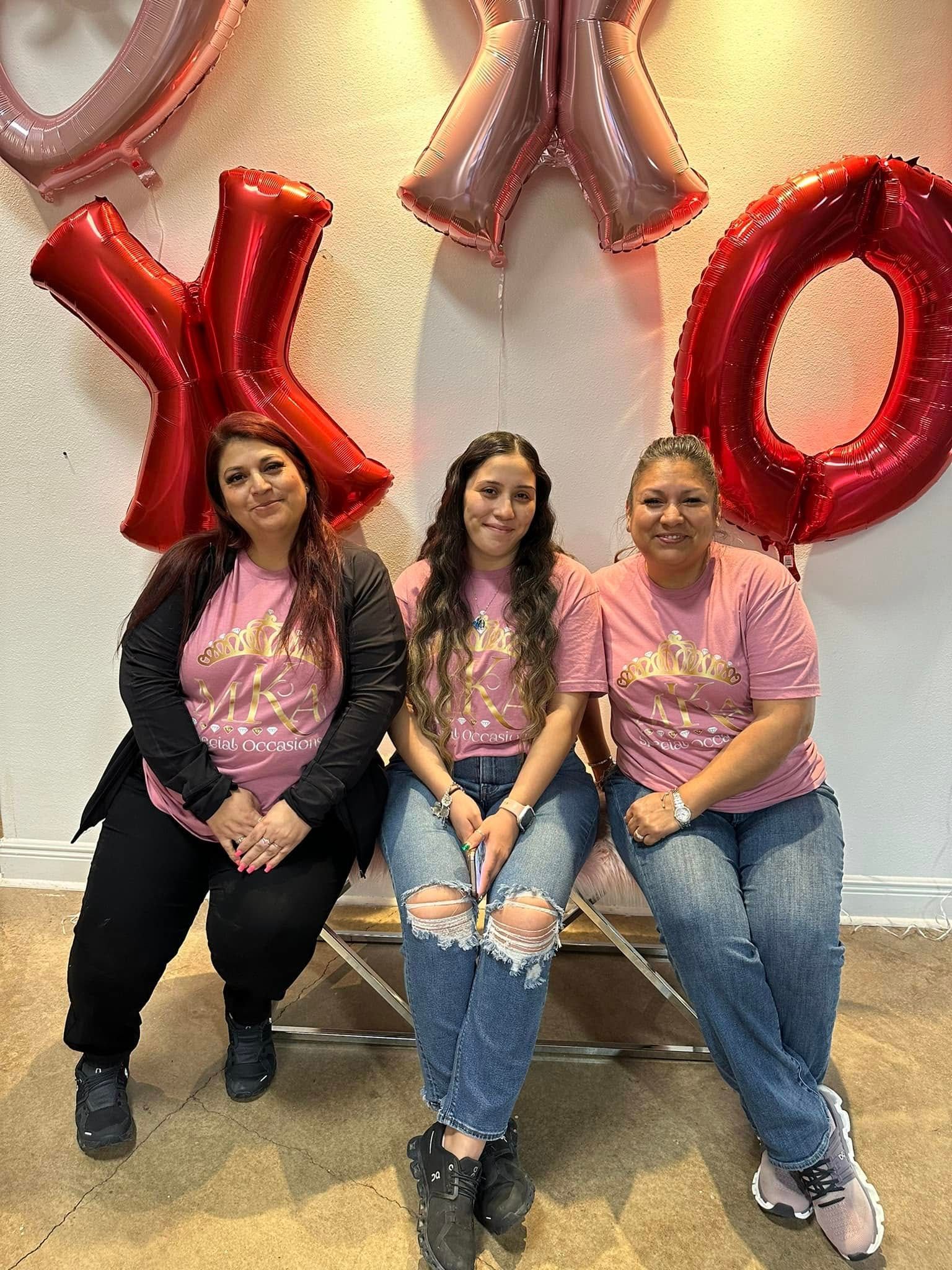 Three women are sitting next to each other in front of balloons.