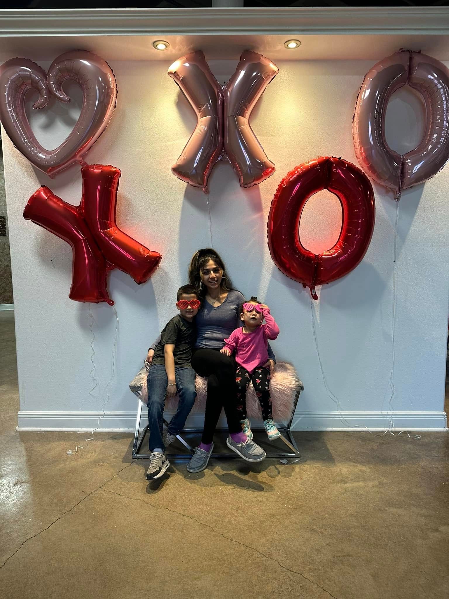 A woman and two children are sitting in front of a wall with balloons on it.