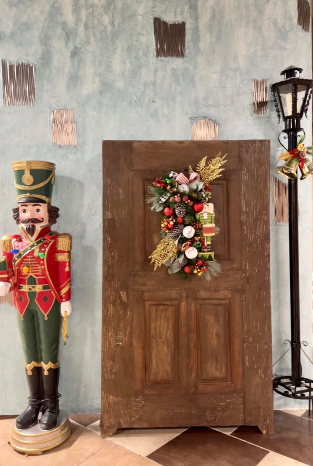 A nutcracker statue is standing next to a wooden door with a christmas wreath on it.