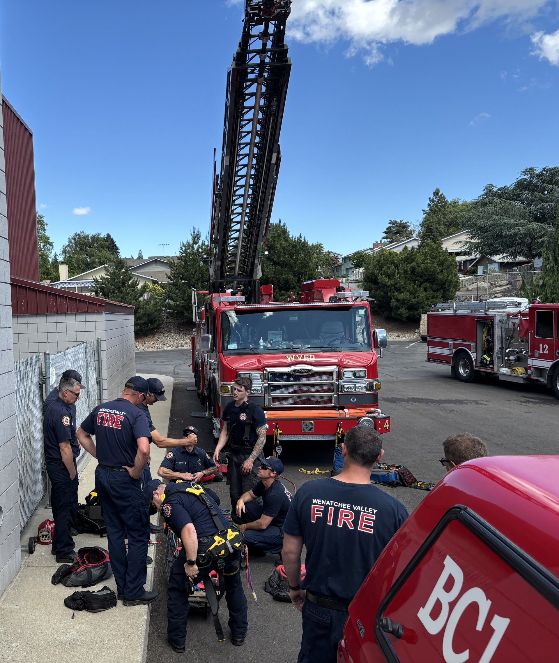 Firefighters attending training next to a firetruck with an extended ladder outdoors under a blue sky.