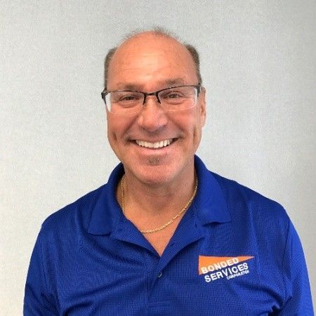 A man wearing glasses and a blue shirt that says bonded services is smiling.