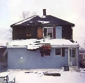 A blue house with a black roof is covered in snow.