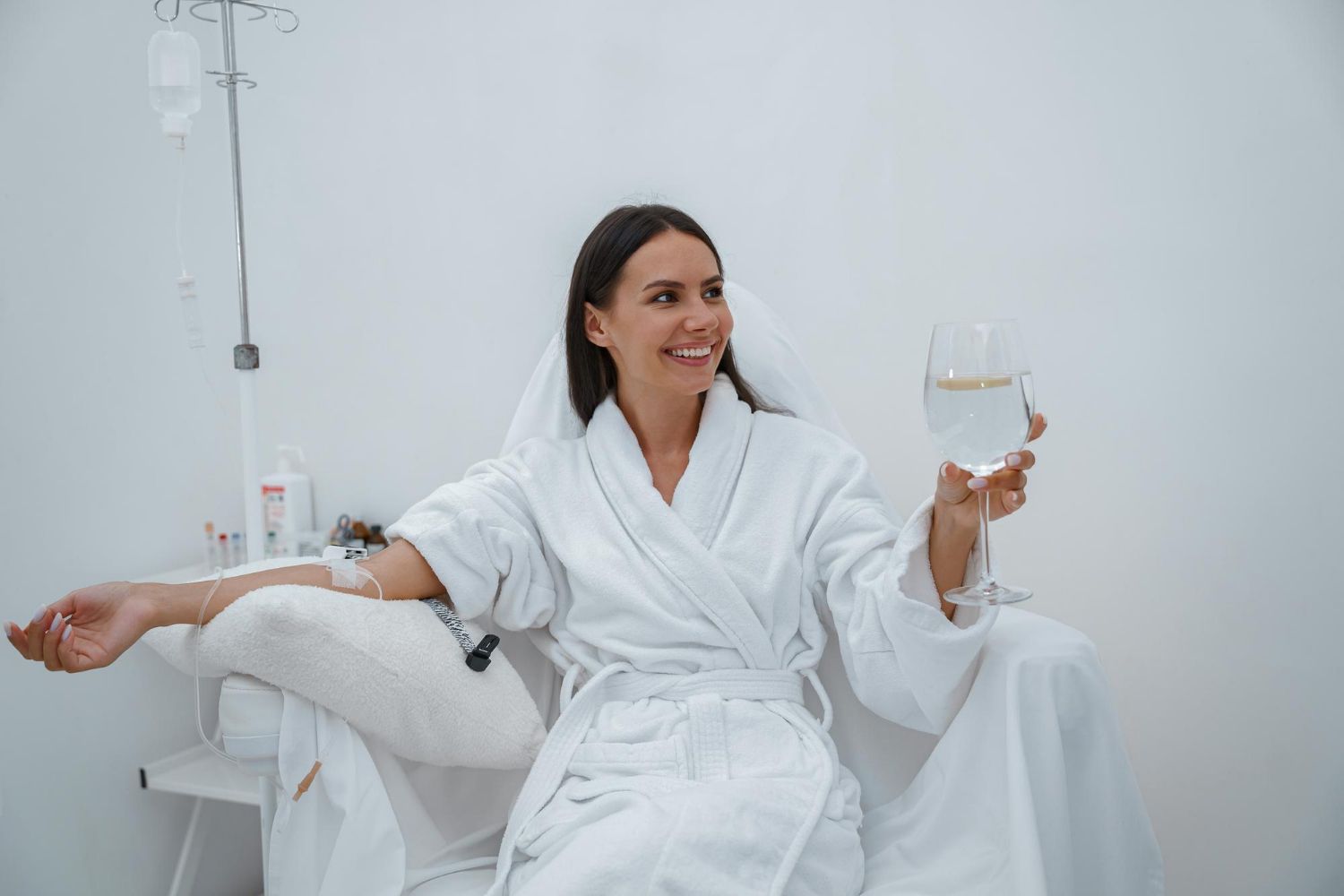 A woman in a bathrobe is sitting in a hospital bed holding a glass of water.
