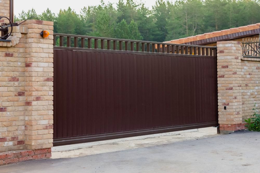 A Brown Sliding Gate Is Open In Front Of A Brick Building — Australian Advanced Fencing In Port Macquarie, NSW