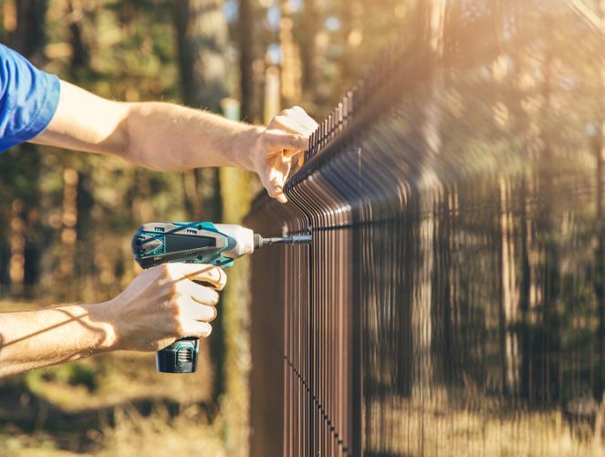 A Man Is Installing A Fence With A Drill — Australian Advanced Fencing In Wauchope, NSW