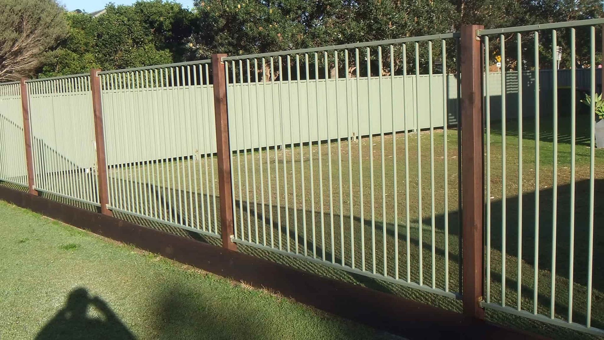 A Metal Fence With Wooden Posts Is Surrounded By Grass And Trees — Australian Advanced Fencing In Port Macquarie, NSW