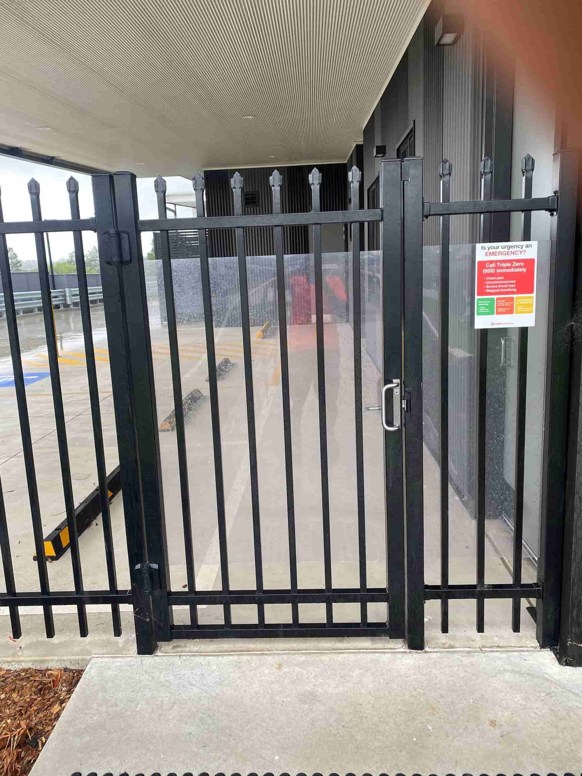 A Black Fence With A Gate In Front Of A Building — Australian Advanced Fencing In Laurieton, NSW