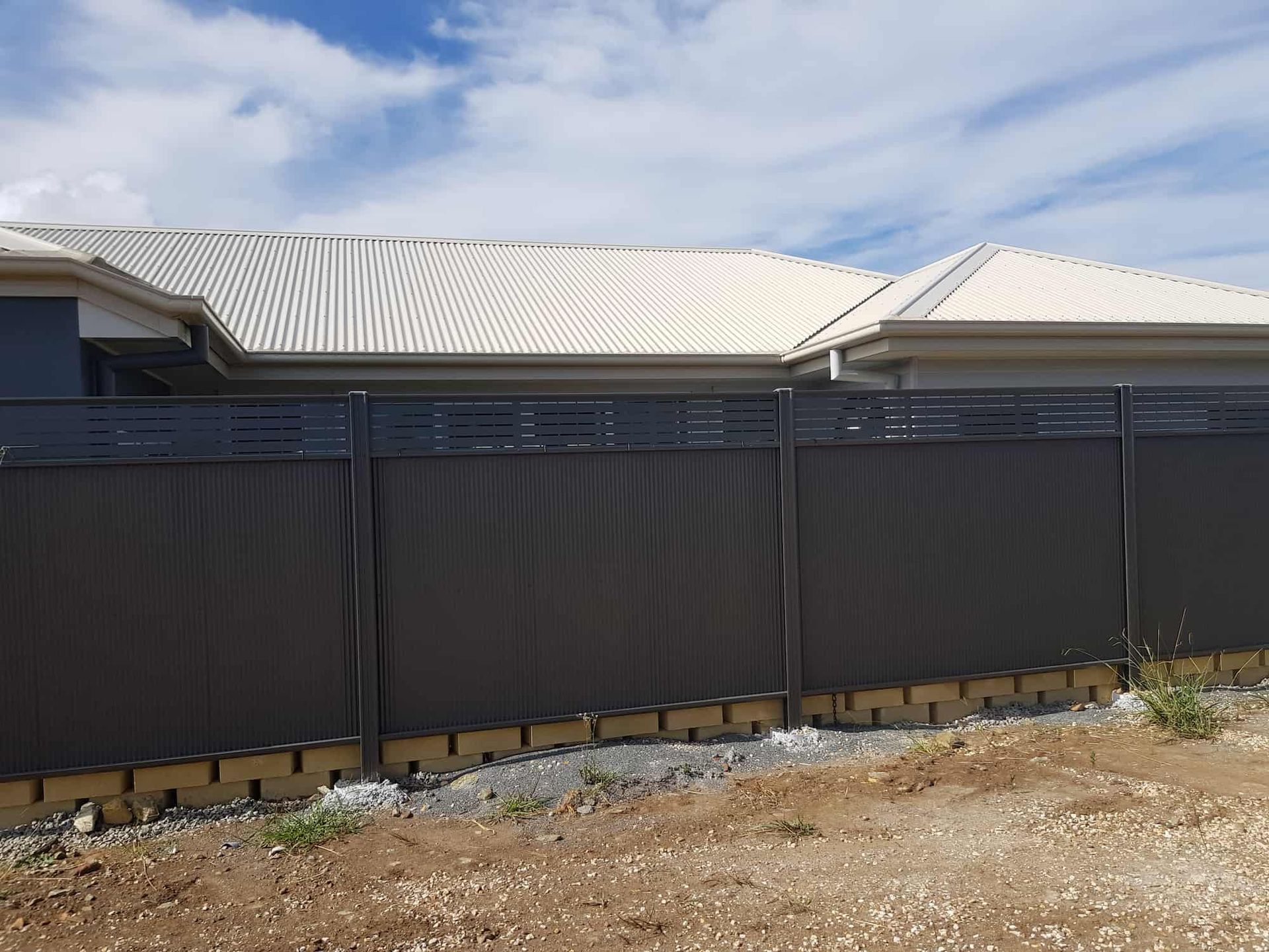 A Black Fence With A Lot Of Rocks Behind It — Australian Advanced Fencing In Wauchope, NSW