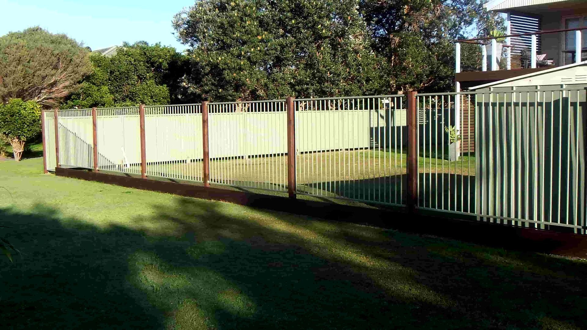 A Fence Surrounds A Lush Green Yard In Front Of A House — Australian Advanced Fencing In Port Macquarie, NSW