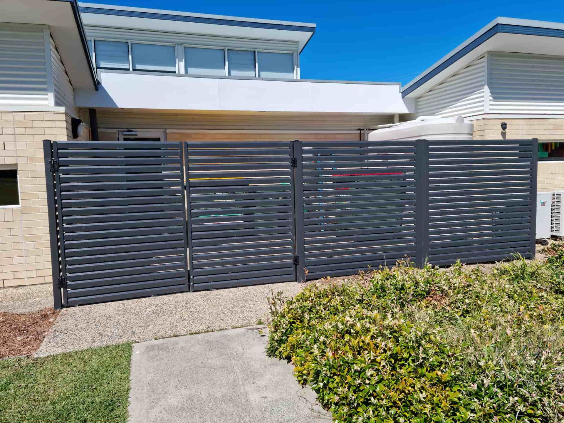A Black Fence Is In Front Of A House — Australian Advanced Fencing In Laurieton, NSW