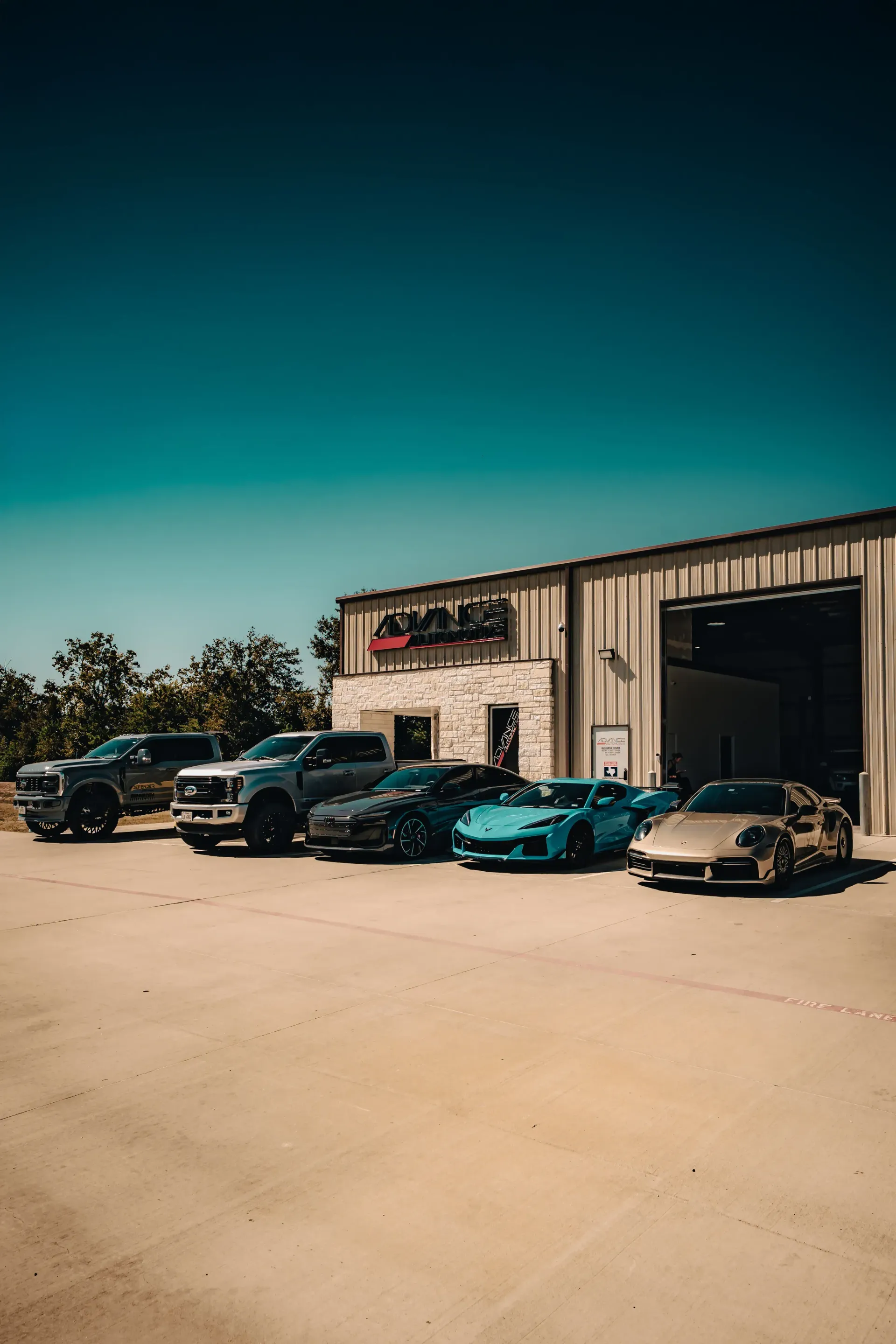 A row of vehicles parked in front of a building with a large open bay door on a sunny day. | Advance Automotive